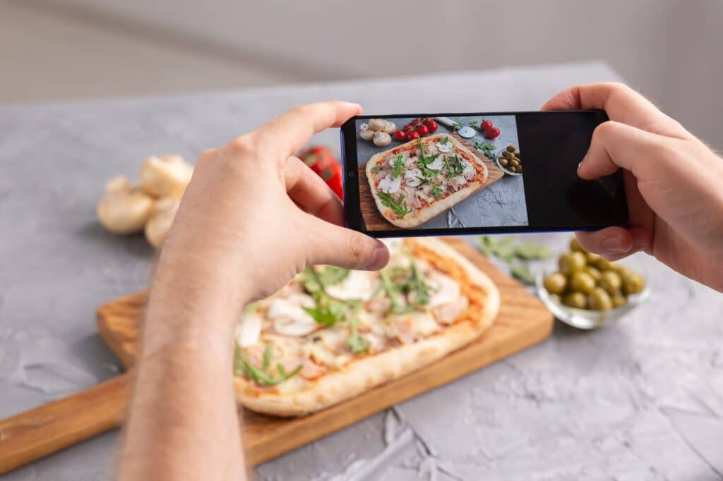 Chef takes pictures of the cooked of italian pizza with parma ham on smartphone. Photographing food