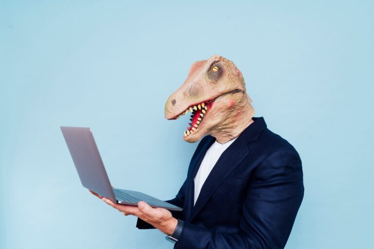 Man with dinosaur mask consulting a laptop computer, blue background
